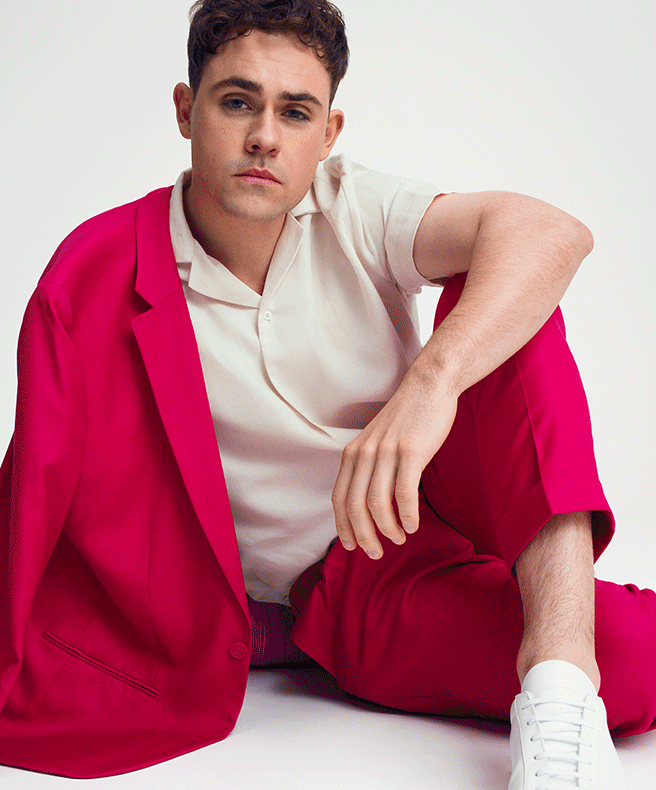 Image of Dacre Montgomery wearing charcoal windowpane suit with blue shirt sitting on char with his legs up and crossed Dacre Montgomery for The Gentle Man