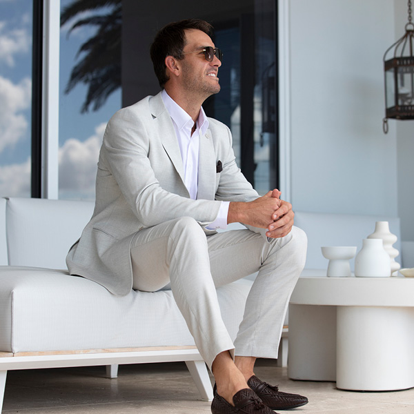 Matt Poole featuring Natural Suit Look Matt Poole seated outdoors wearing cream Natural Suit Look, white shirt, brown loafers and sunglasses smiling looking away