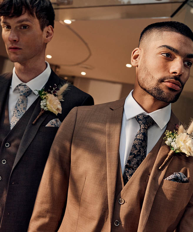 Two male models walking through doorway wearing POLITIX brown suits and corsage