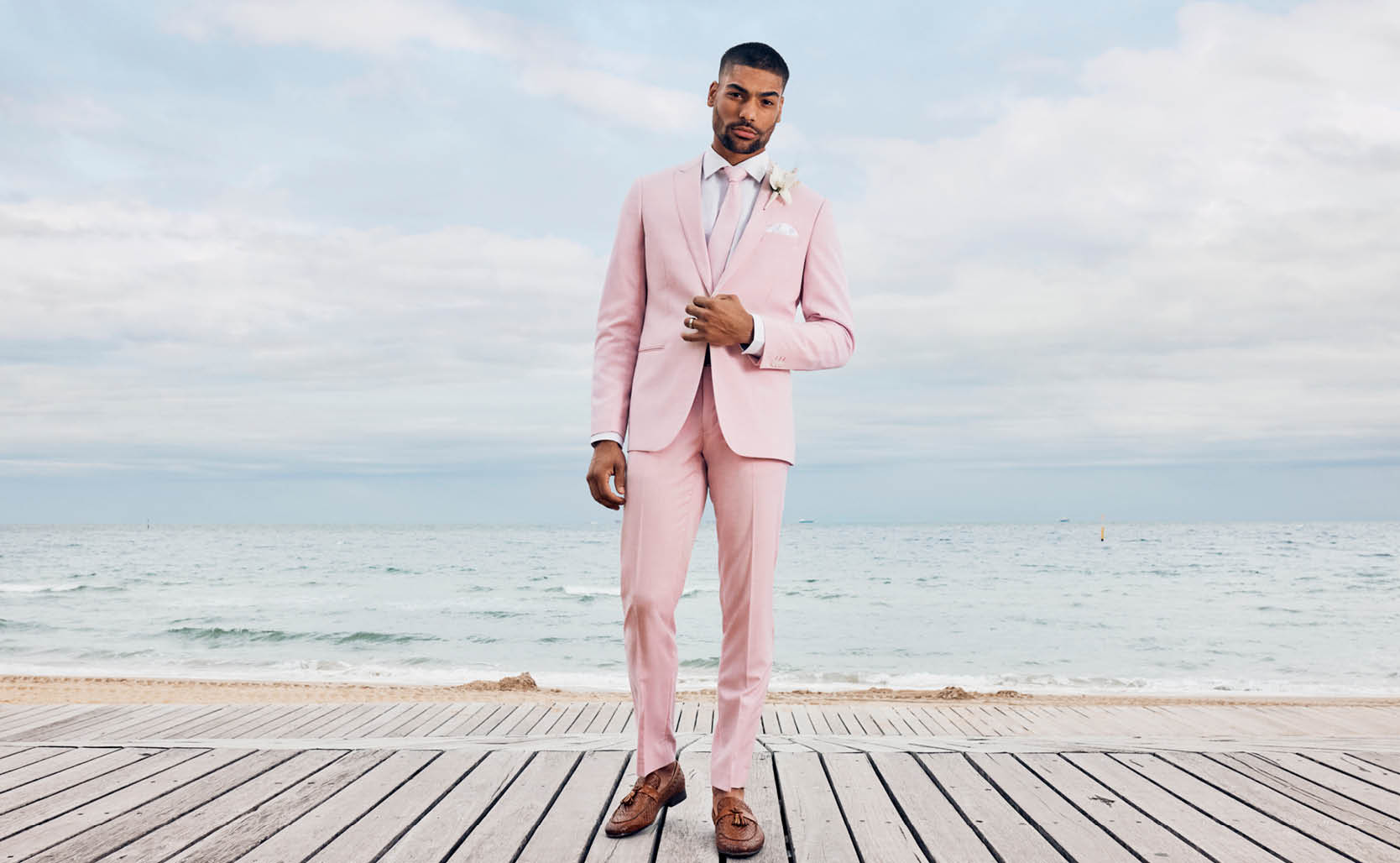 Male model wearing POLITIX pink suit and white shirt on beach boardwalk in front of ocean