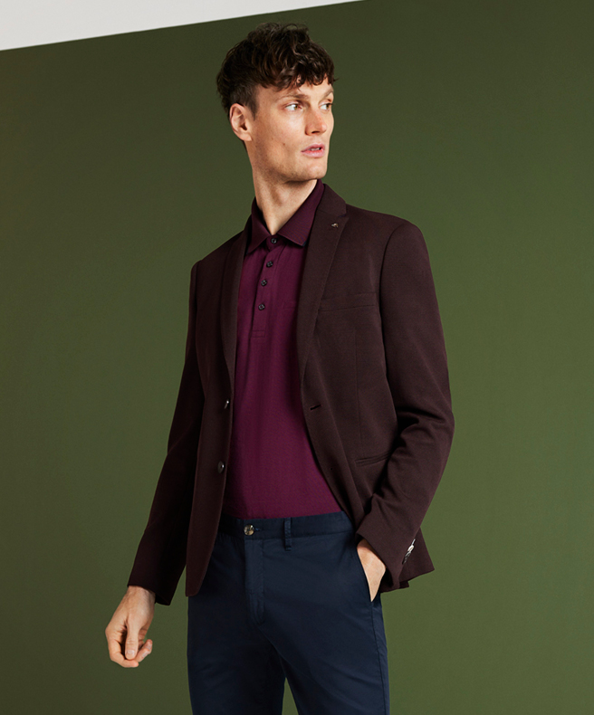 Model standing in front of green background wall wearing Claret Knitted Blazer, Burgundy polo and Navy Chinos