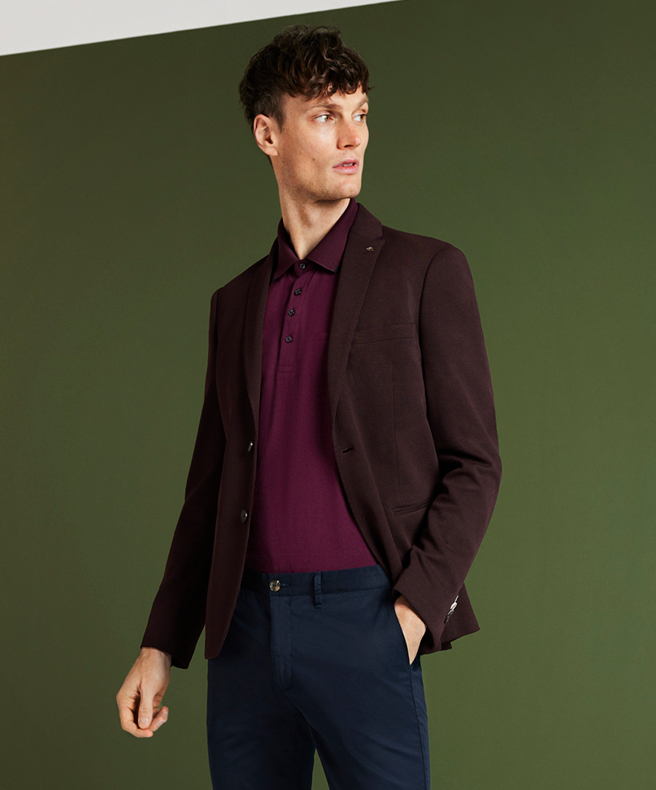 Make your mark with a knitted blazer Model standing in front of green background wall wearing Claret Knitted Blazer, Burgundy polo and Navy Chinos