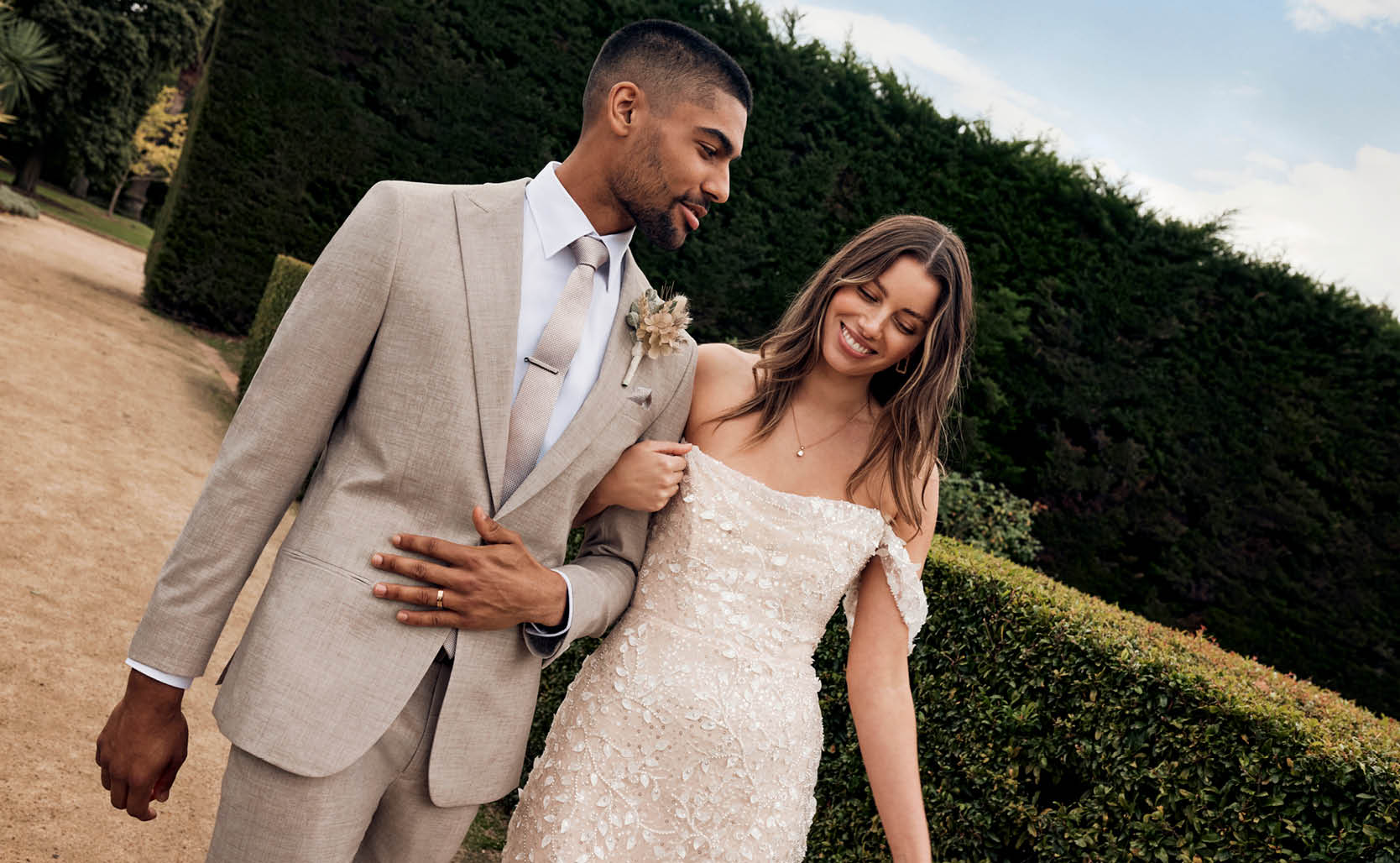 What to wear to a wedding Male model wearing beige POLITIX suit with female model walking in a garden setting