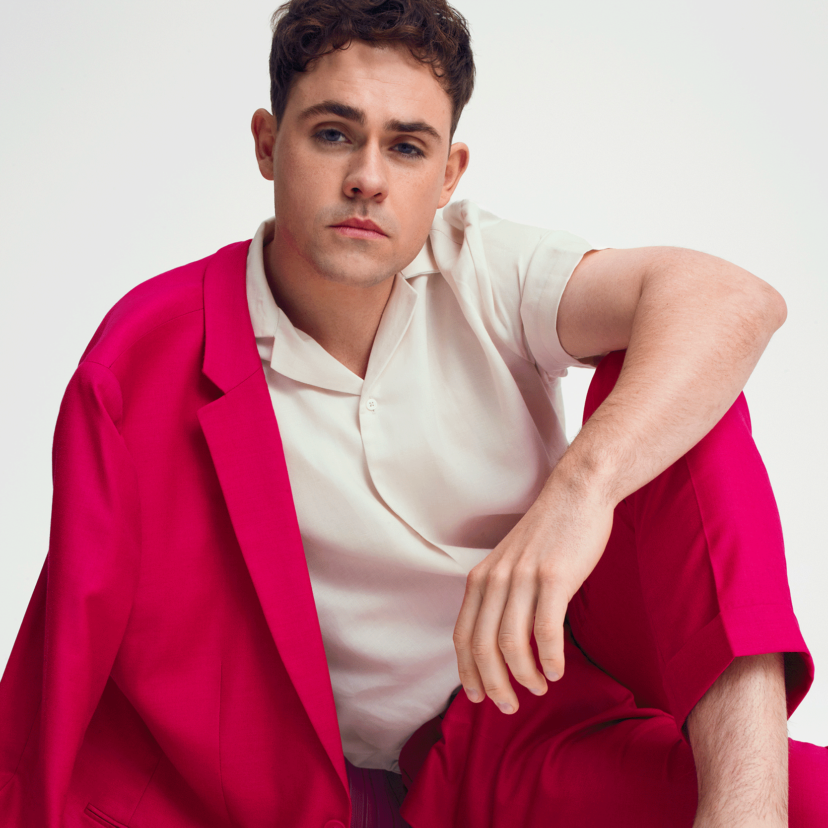 Image of Dacre Montgomery wearing charcoal windowpane suit with blue shirt sitting on char with his legs up and crossed Dacre Montgomery for The Gentle Man