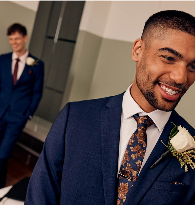 Male model smiling in foreground wearing POLITIX Navy suit with second male model in background wearing POLITIX navy blue suit
