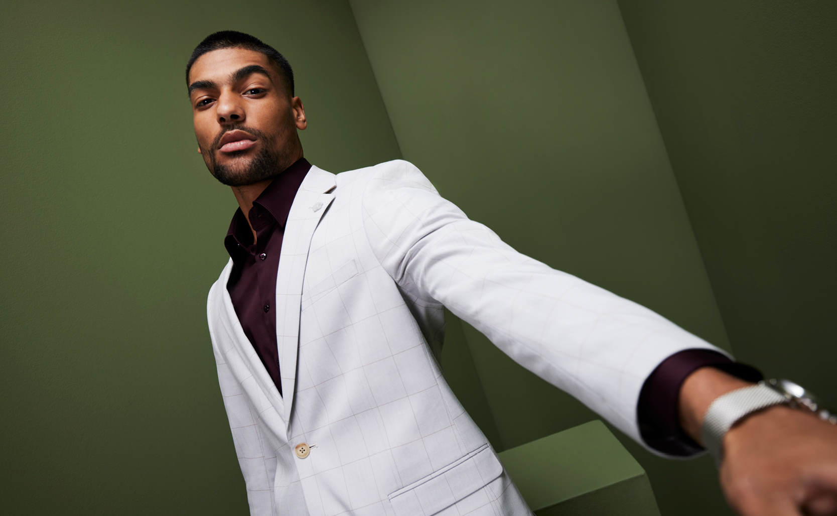 Pick a Tone That Shouts You Model standing in front of a green wall background wearing POLITIx White windowpane suit with burgundy button up shirt