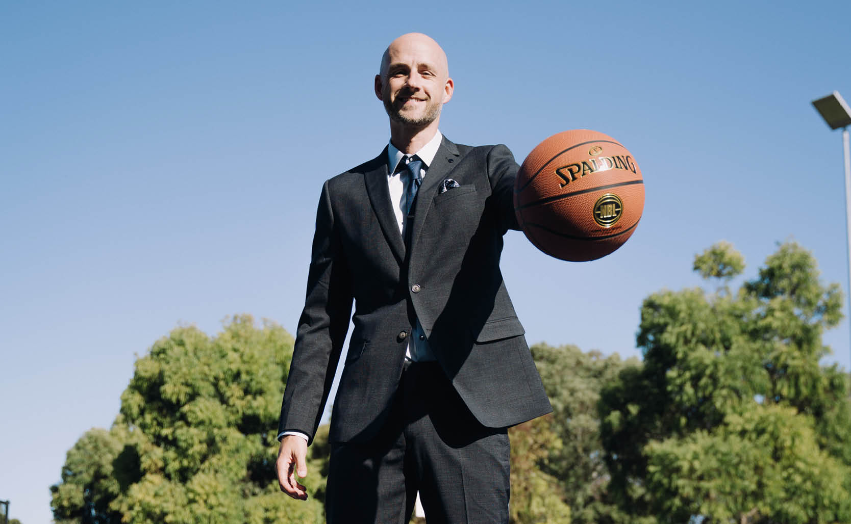 Jarrod walsh outside on basketball court  in suit holding basketball